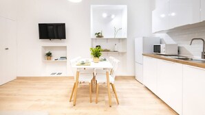A modern kitchen with white cabinetry, a dining table with chairs, a TV mounted on the wall, and a microwave on the countertop.