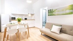 A modern kitchen with white cabinets, a dining table with chairs, a sofa, and a painting of bamboo on the wall.