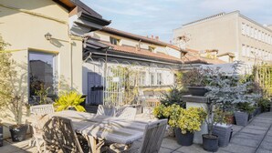 A courtyard with a wooden table and chairs, surrounded by potted plants and a metal fence. - Easylife - Amazing studio in San Babila (Milano)