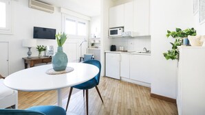 A modern kitchen with white cabinets, a microwave, and a sink. There is a dining table with chairs and a vase with flowers. - Easylife - Amazing studio in San Babila (Milano)