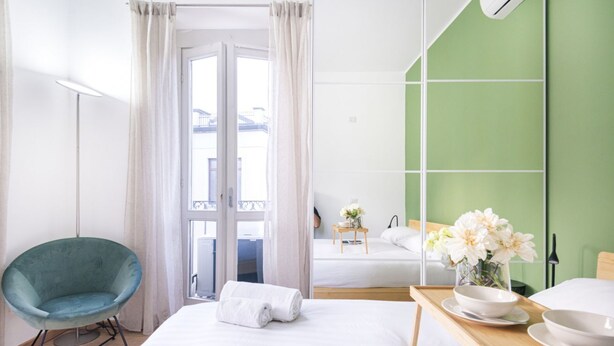 A hotel room with a bed, a chair, a bedside table with a bowl and flowers, and a green wall.