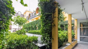 Um pátio com um edifício amarelo, vegetação e uma galeria coberta.