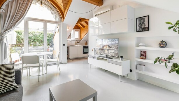 Uma sala de estar moderna com uma televisão grande, móveis brancos e vista para o exterior.