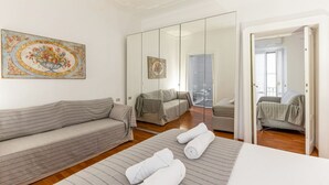 A modern hotel room with a sofa, a bed, and a large mirror reflecting the room.