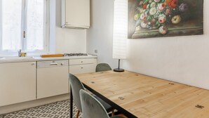 A modern kitchen with white cabinets, a wooden dining table, and a painting of flowers on the wall.