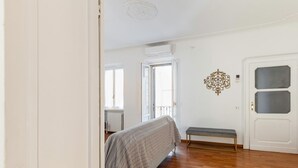 A room with a bed, a bench, a door, and a wall decoration.
