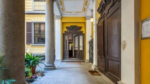 Un pasillo con columnas, pared amarilla y puerta de madera.