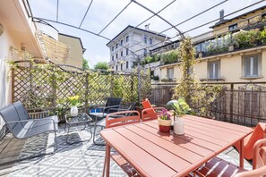 A patio with a red table and chairs, a patterned rug, and a lattice fence with climbing plants.