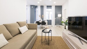 Un salon moderne avec un canapé beige, une table basse, un téléviseur à écran plat et un coin repas comprenant des chaises et une table.