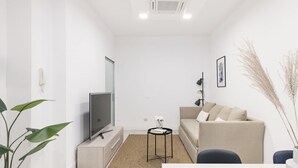 Un salon moderne avec un téléviseur à écran plat, un canapé beige, une petite table ronde et une plante en pot.