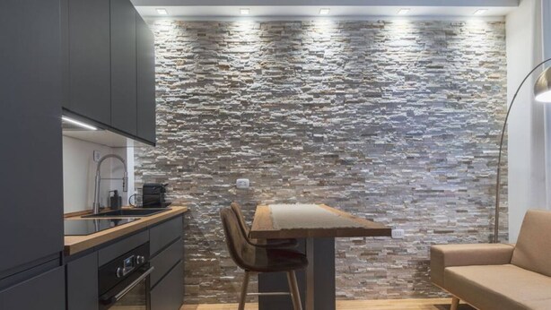 Una cocina moderna con protector mural de piedra, una mesa de comedor de madera y un sofá.