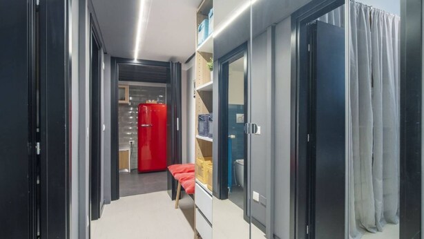 Un pasillo moderno con un perchero rojo, una mesita con una cesta, y una puerta que da a un baño.