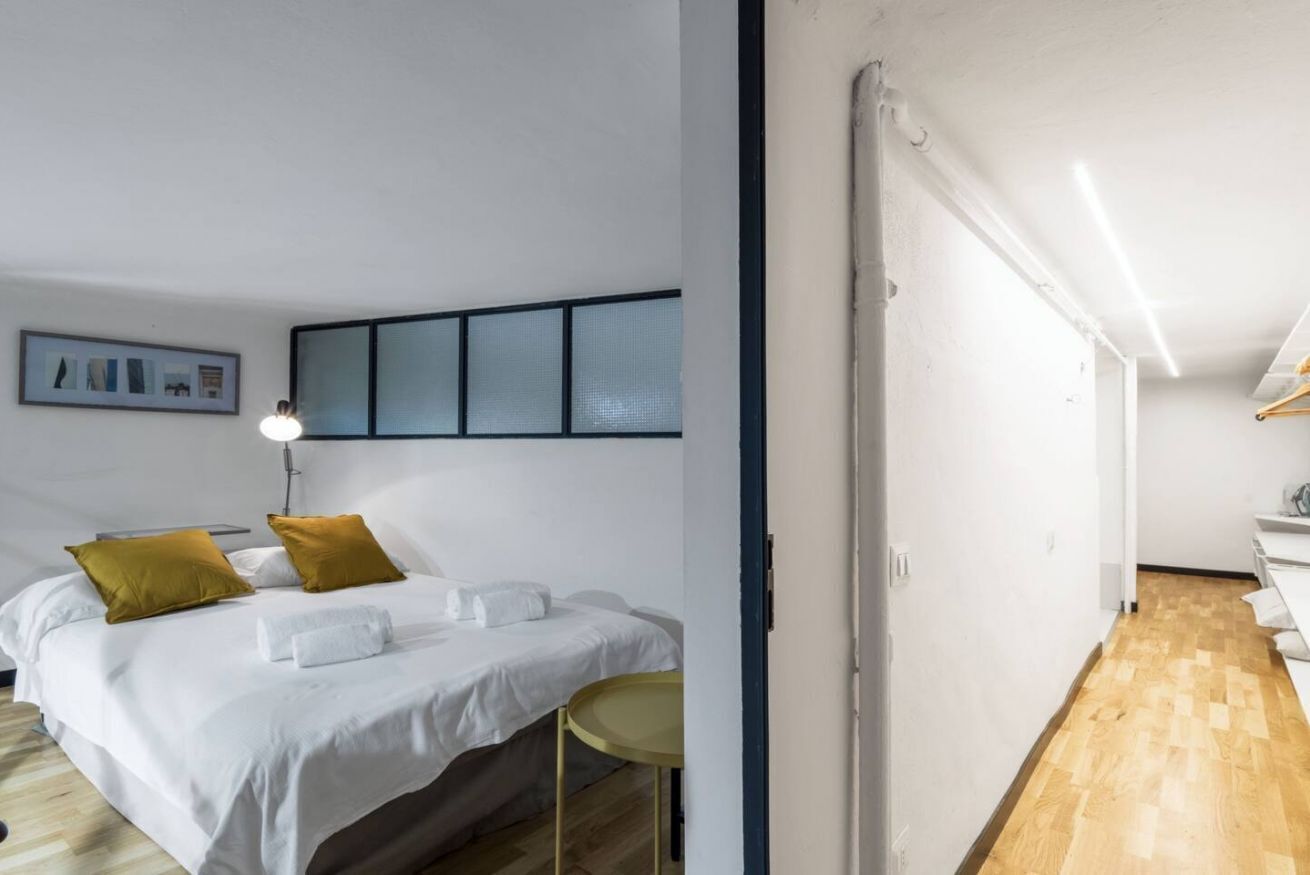 Une chambre d’hôtel moderne, équipée d’un lit, d’une petite table ronde et d’un luminaire fixé au mur.