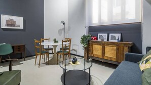 Una sala de estar moderna con una mesa de centro de vidrio, sillas de madera, un sofá y un aparador de madera con cuadros enmarcados.