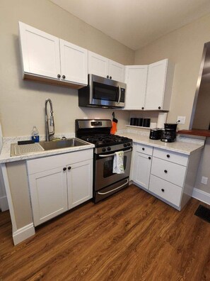 A compact kitchen with white cabinets, a stainless steel stove, a microwave, and a sink.
