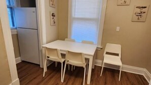 A small dining area with a white table and four chairs, a window with blinds, and a refrigerator in the adjacent kitchen. - Cleneay #1, Private 3 Bed near Xavier & Downton (Cincinnati)