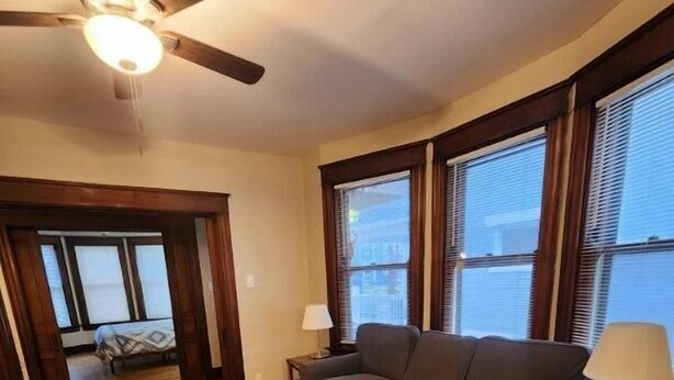 A living room with a wooden floor, a gray sofa, a wooden coffee table, and a ceiling fan. - Cleneay #1, Private 3 Bed near Xavier & Downton (Cincinnati)