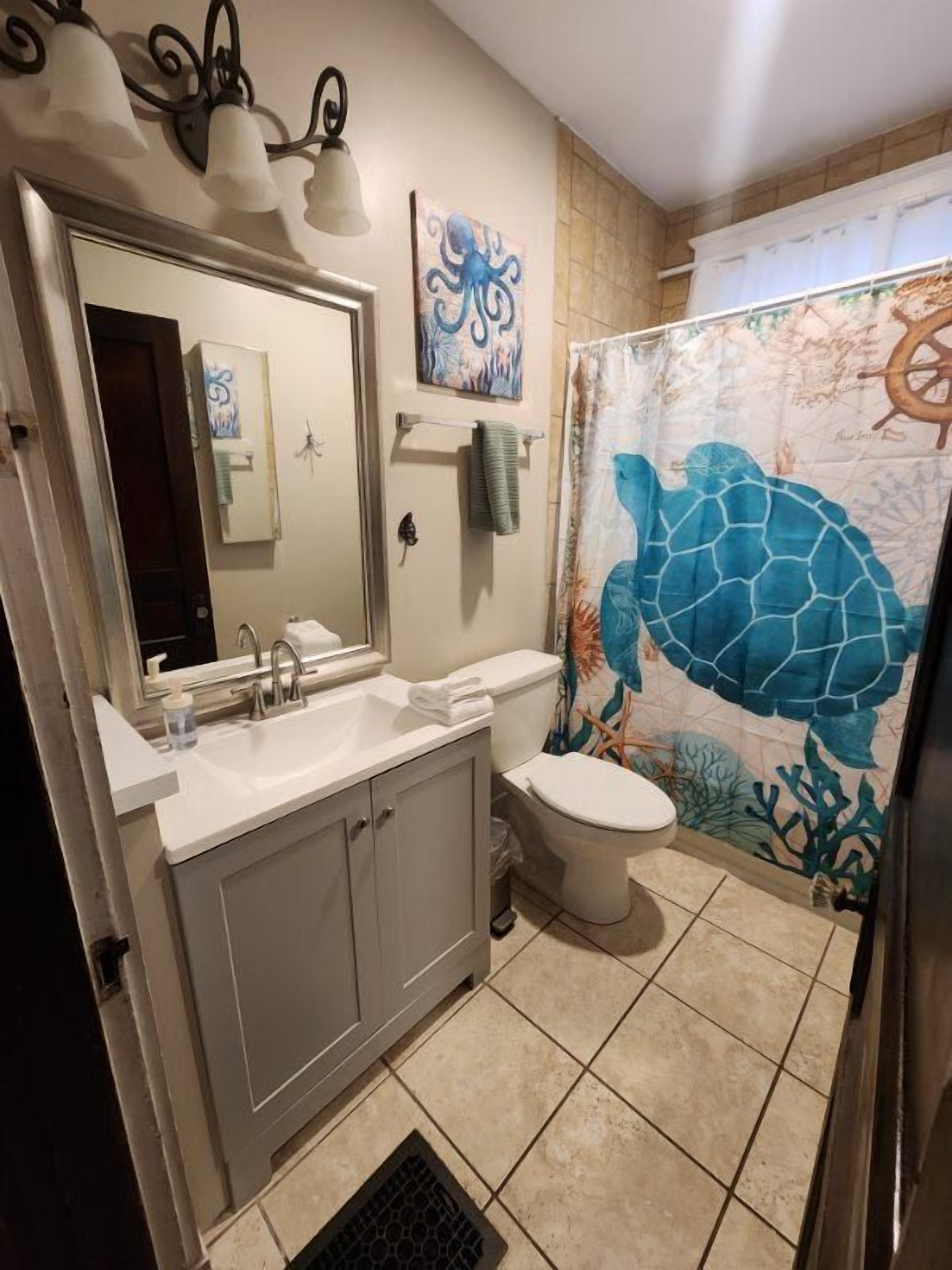 A bathroom with a sink, toilet, and shower curtain featuring a sea turtle design.