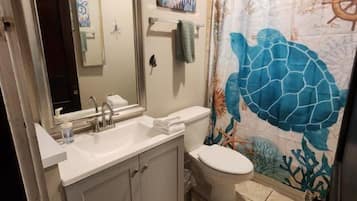 A bathroom with a sink, toilet, and shower curtain featuring a sea turtle design.