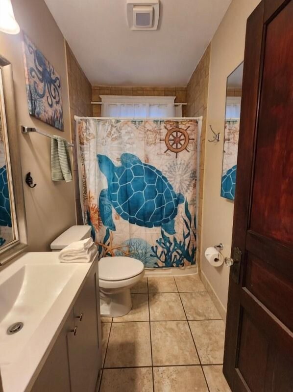 A bathroom with a bathtub, toilet, and shower curtain featuring a sea turtle design.