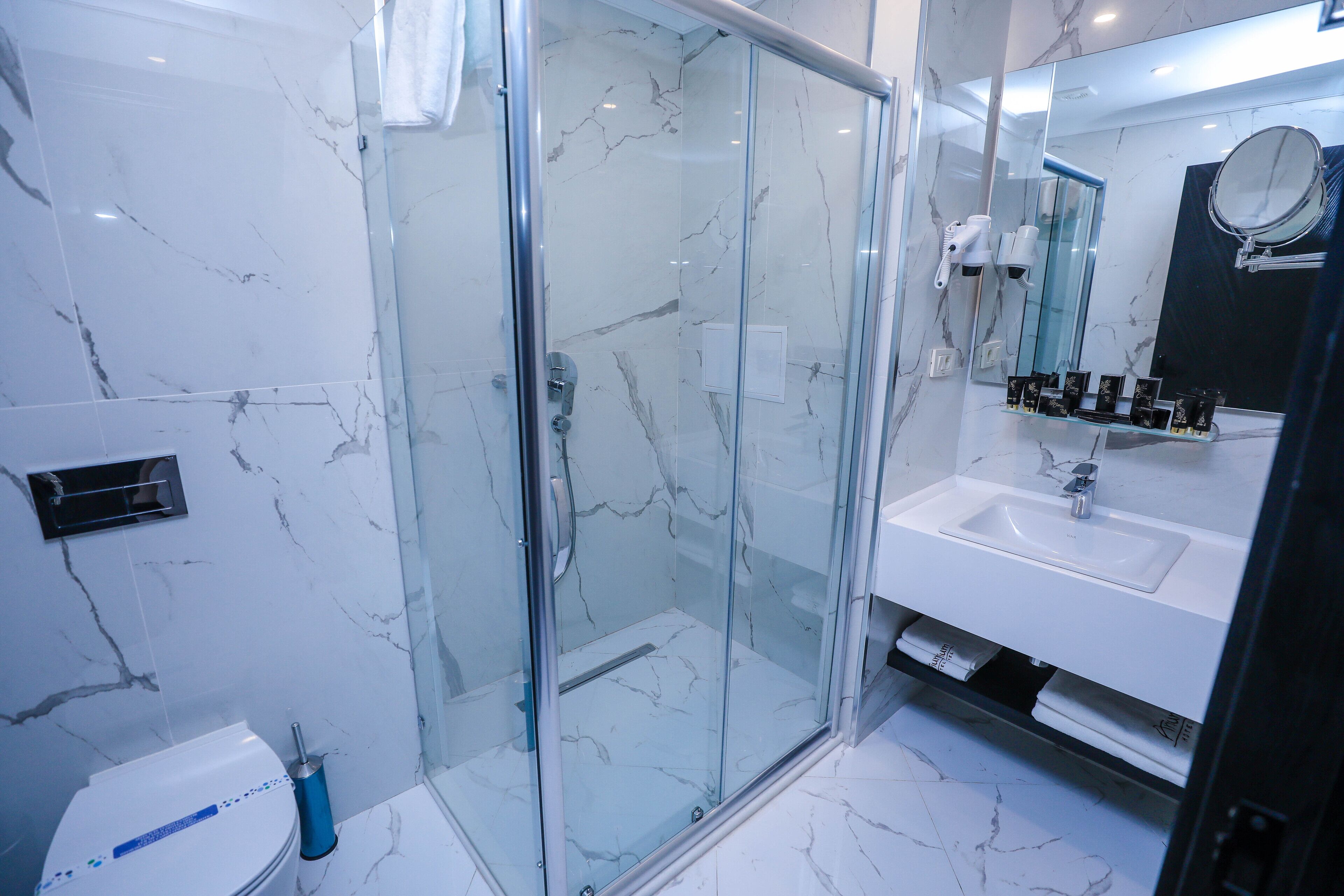 A modern bathroom with a glass-enclosed shower, a white sink, and a marble-tiled floor.