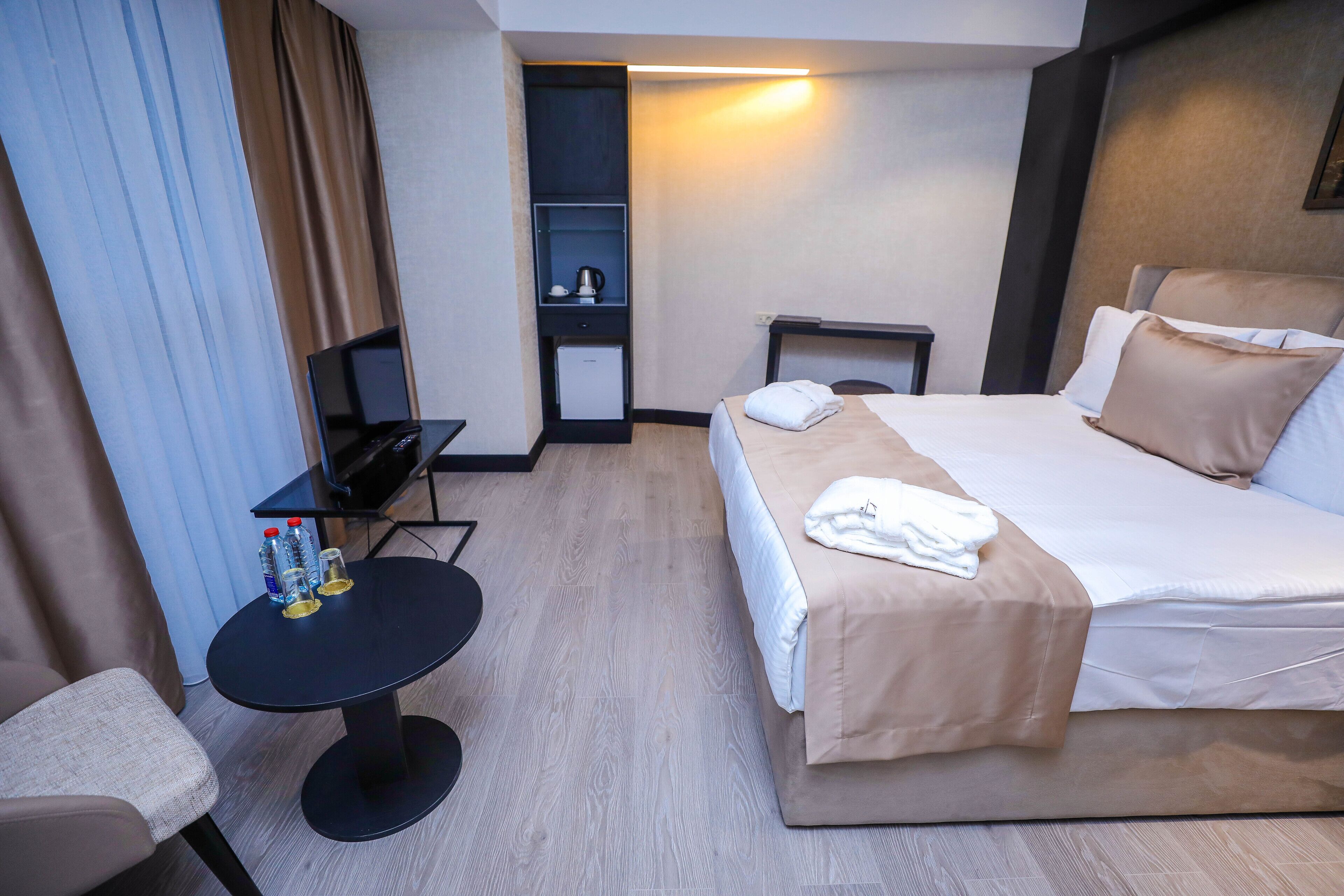 Hotellihuone, jossa on sänky, työpöytä, tuoli, pieni pöytä pulloineen ja televisio.