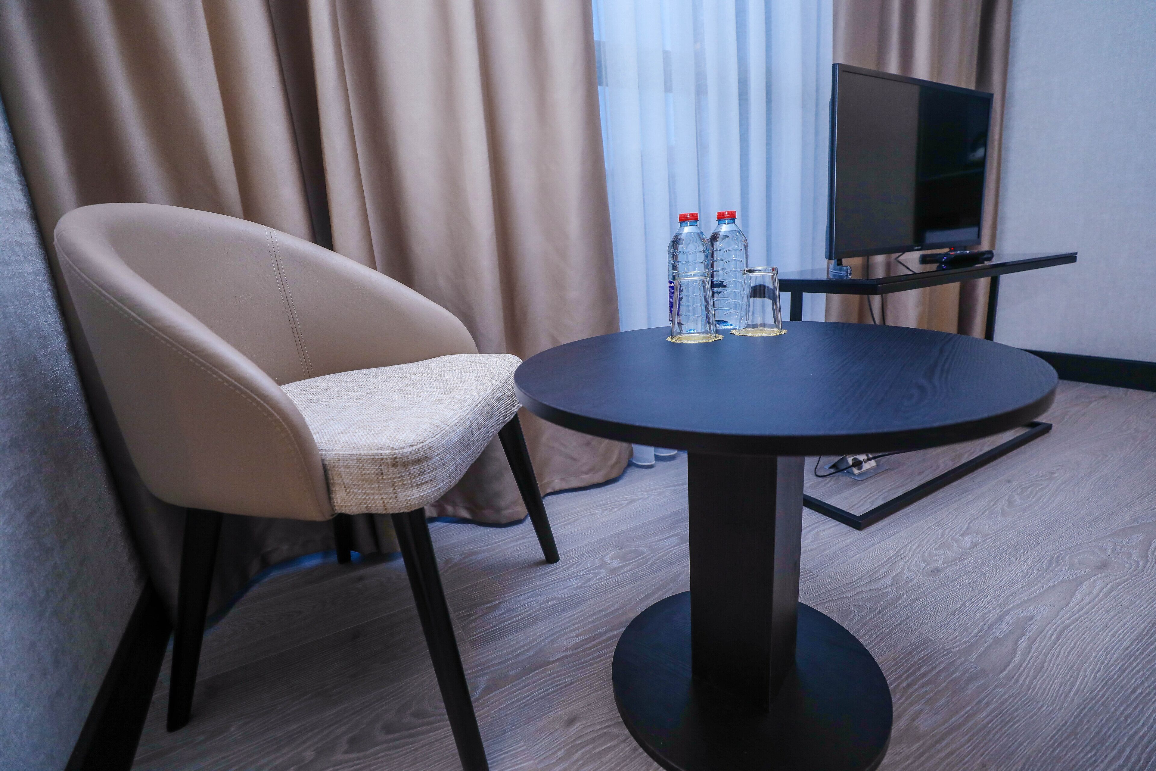 A hotel room with a round table, a TV on a stand, and a chair.
