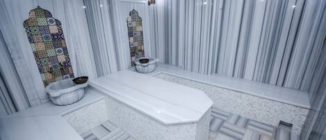 A bathroom with a marble floor, a bathtub, and a window with a decorative pattern.