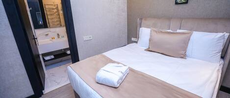 Una cama bien tendida con edredón color crema y blanco, una toalla blanca sobre la cama y un cuadro colgado en la pared.