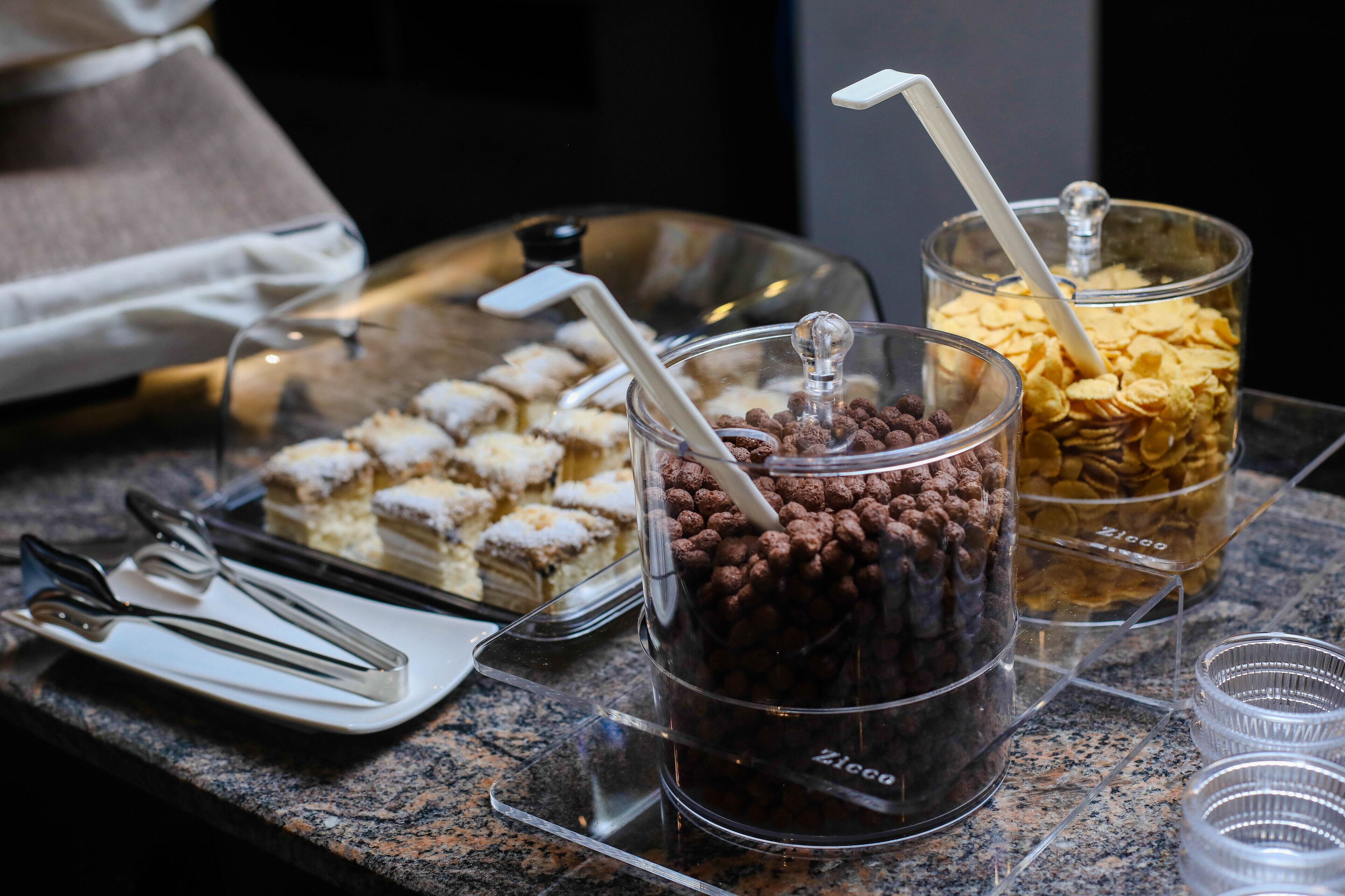 A buffet table with various desserts and snacks, including a glass jar of chocolate balls and a container of cereal.