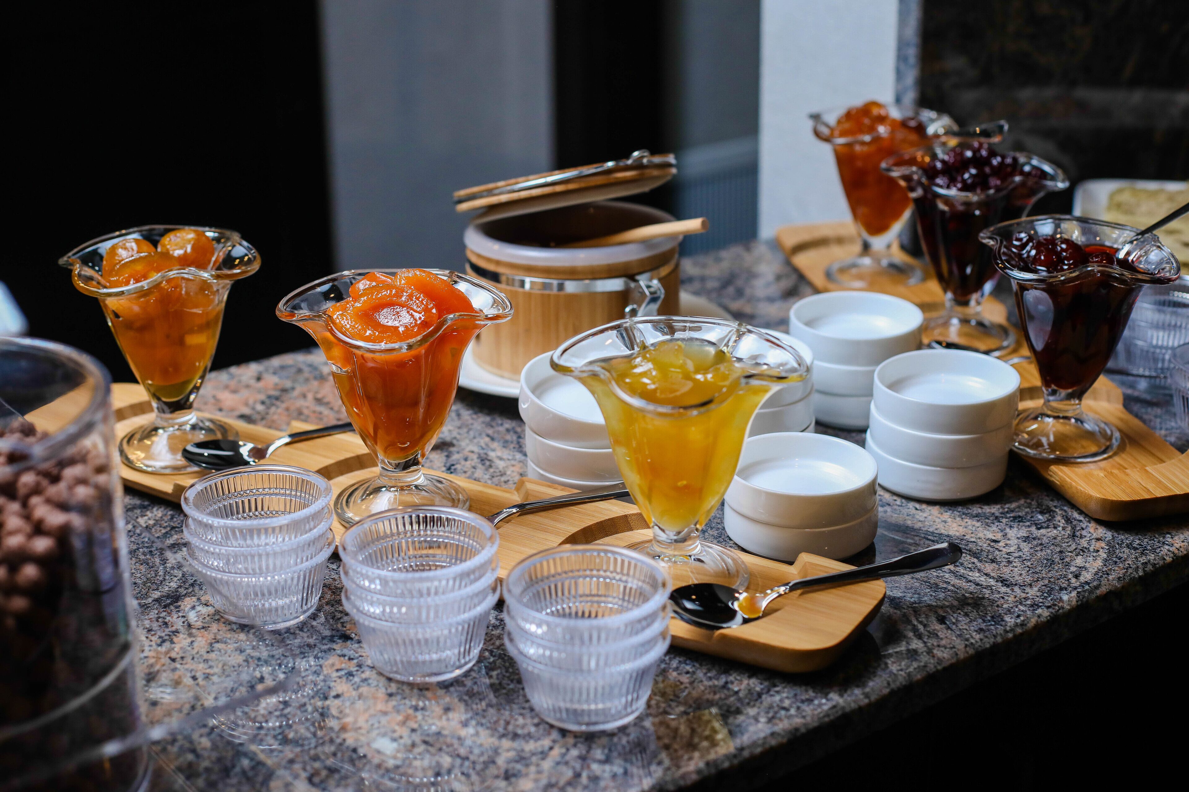 A buffet table with various food and drink items, including fruit, desserts, and beverages in clear glasses and bowls.