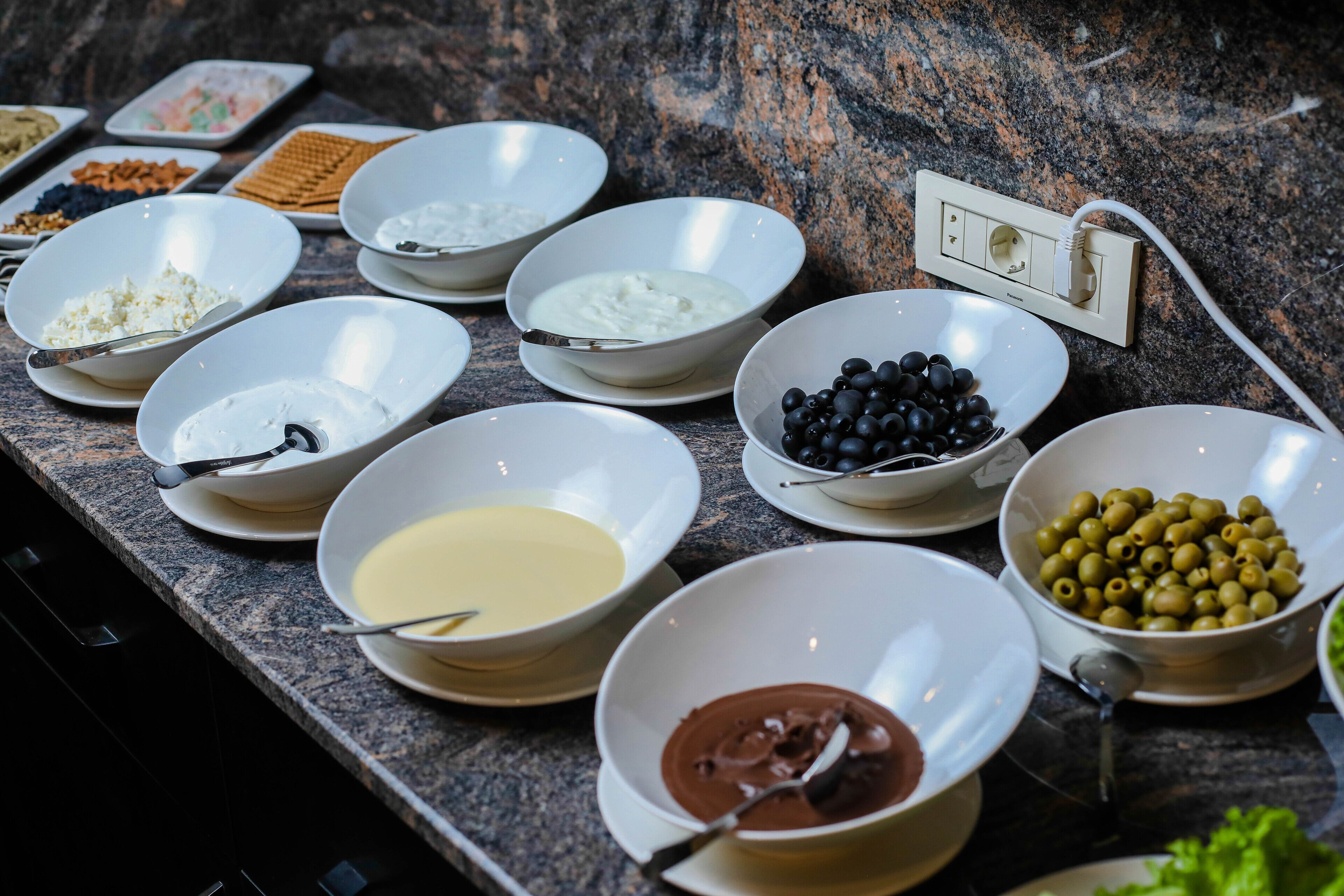 A buffet table with various food items including bowls of yogurt, chocolate sauce, olives, and other snacks.