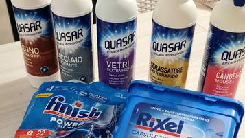 Un plan de travail de cuisine avec divers produits de nettoyage, notamment des bouteilles de la marque Quasar et un récipient bleu contenant du produit concentré Rixe.
