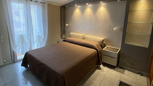 Une chambre à coucher avec un lit, des rideaux, une table de chevet et une étagère fixée au mur.