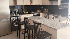 Una cocina moderna con una isla central, taburetes de bar, lavadora y horno empotrado.