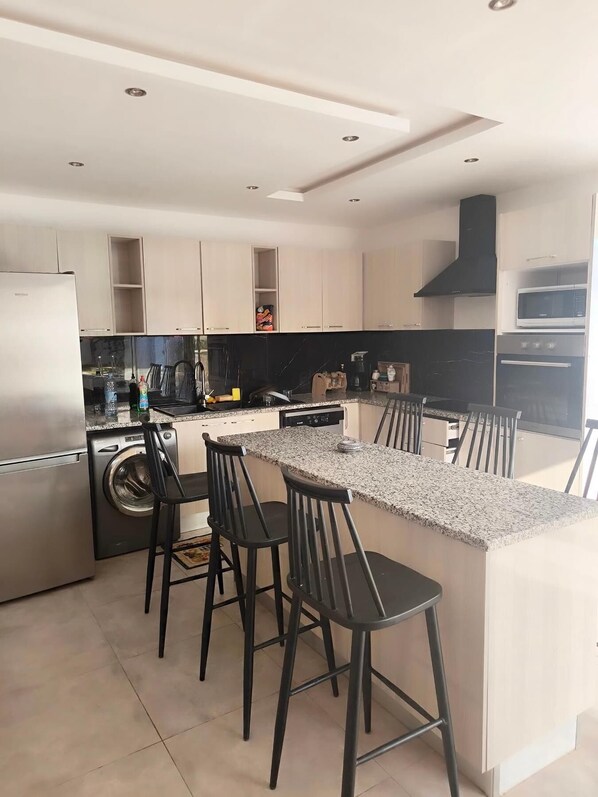 Uma cozinha moderna com uma ilha central, banquetas, máquina de lavar e forno embutido.