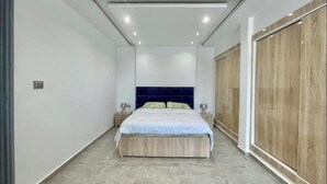 Un dormitorio con cama, mesitas de noche, un armario de madera y un cabecero azul.