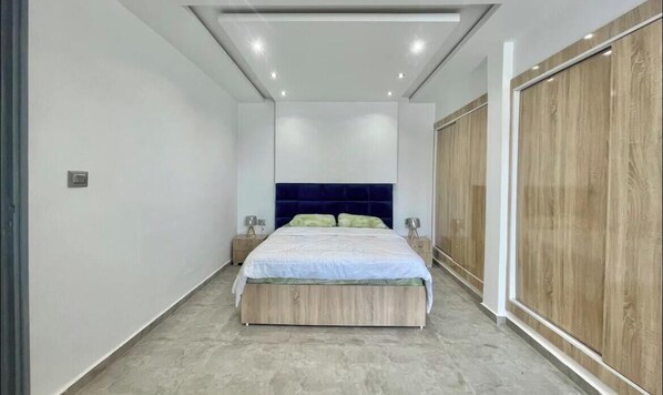 Ein Schlafzimmer mit einem Bett, Nachttischen, einem Holzschrank und einem blauen Kopfteil.