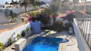 Una piscina rectangular con interior azul, rodeada por un muro blanco y un suelo de baldosas.