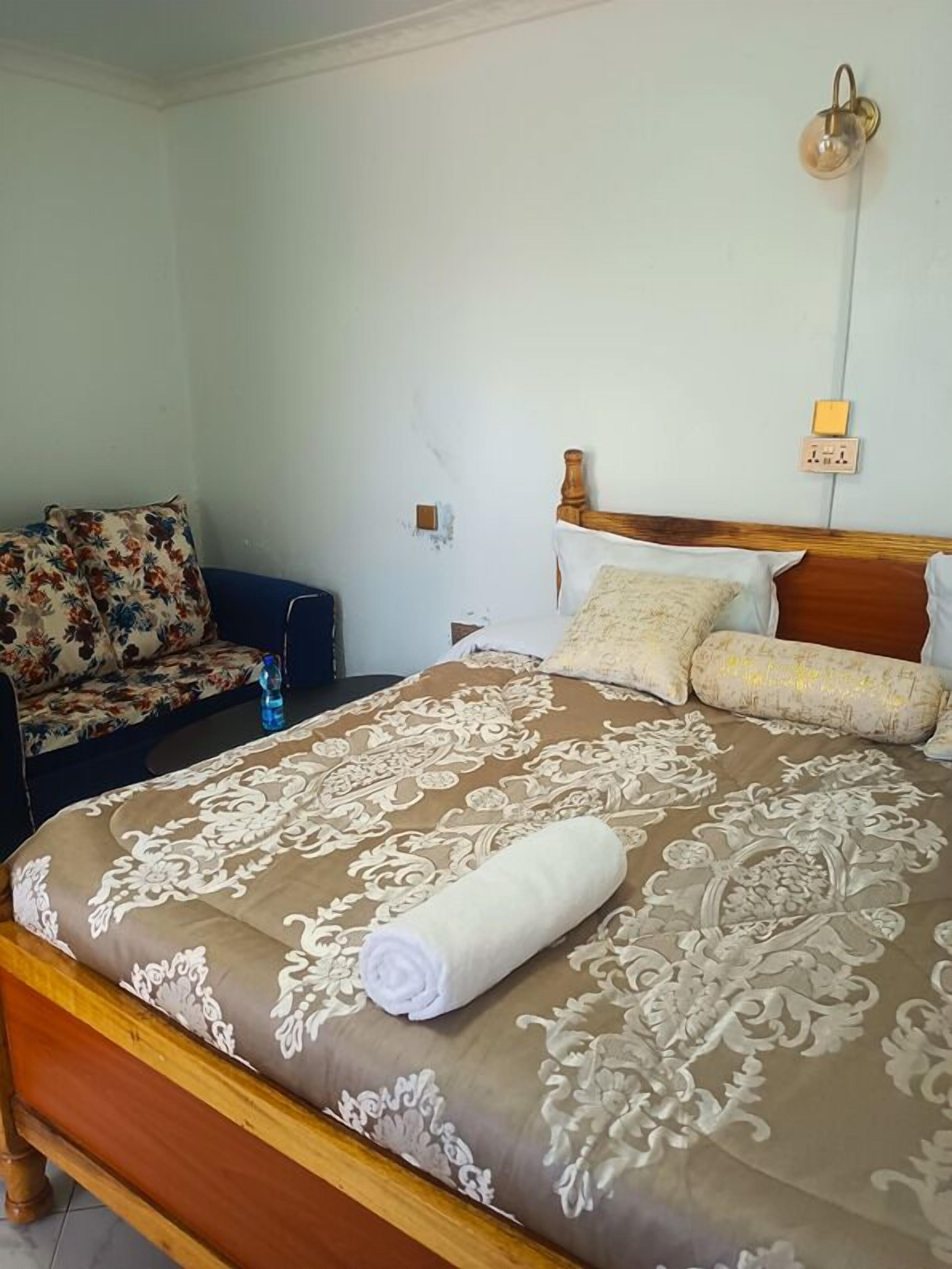 A neatly made bed with a patterned bedspread, a wooden headboard, and a rolled towel on the bed.