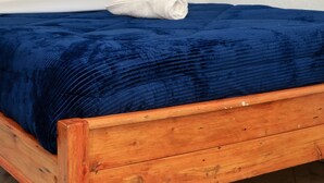 Una cama con una manta azul y almohadas blancas, un cabecero de madera y una pared con cortinas estampadas.