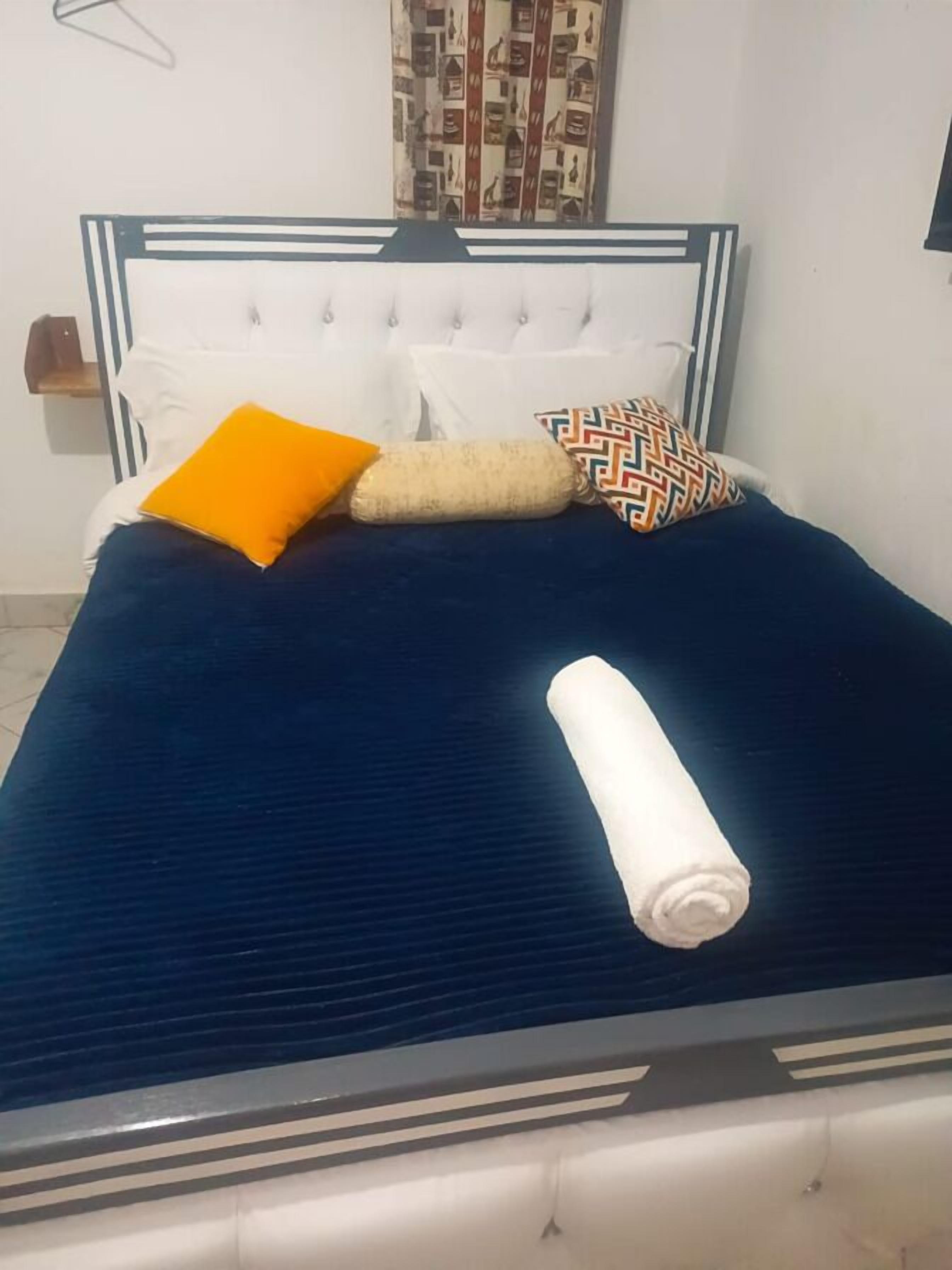 A bed with a dark blue bedspread, white pillows, and a rolled white blanket.