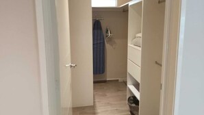 Kapea käytävä, jossa on puulattia. Vasemmalla puolella on valkoinen ovi ja oikealla puolella valkoisilla hyllyillä varustettu vaatekaappi.