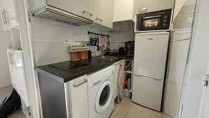 Eine kompakte Küche mit Waschmaschine, Mikrowelle und Kaffeemaschine.