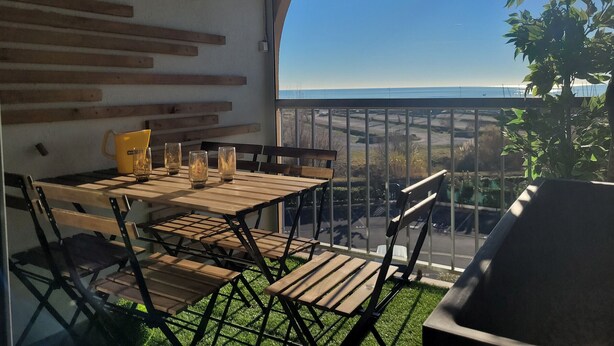 Ein Balkon mit Holztisch und Stühlen, einer gelben Tasse und einem Glas.