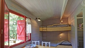 A compact room with a wooden table, white chairs, a bunk bed, and a window with red shutters. - Charming caravan for 4 guests with pets allowed, linens and cleaning included (Saint-Germain-Lespinasse)