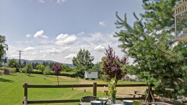 A wooden deck with a table and chairs, overlooking a grassy area with trees and a small shed. - Charming caravan for 4 guests with pets allowed, linens and cleaning included (Saint-Germain-Lespinasse)