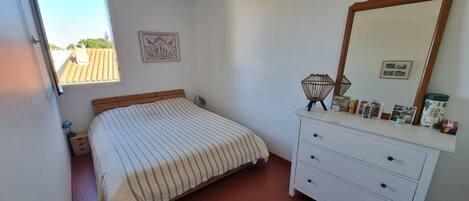 A bedroom with a bed, a dresser, a mirror, and a window.
