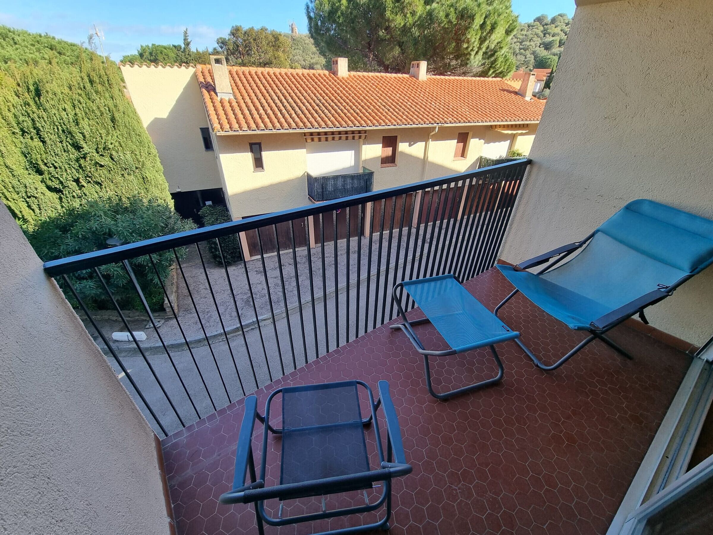 A balcony with two blue lounge chairs and a small table, surrounded by a metal railing.