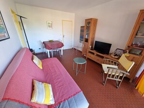 A room with a bed, a TV, a wooden cabinet, and a dining table with chairs. - Charming secure T2 in Collioure with parking near the beach (Collioure)